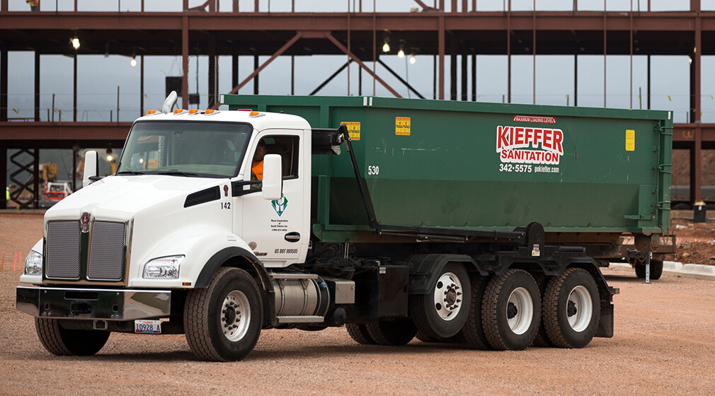 Photo of a Kieffer Sanitation truck with a roll-off bin ready for delivery.